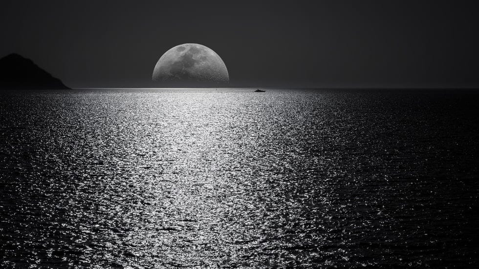 moon over the ocean with boat in the distance